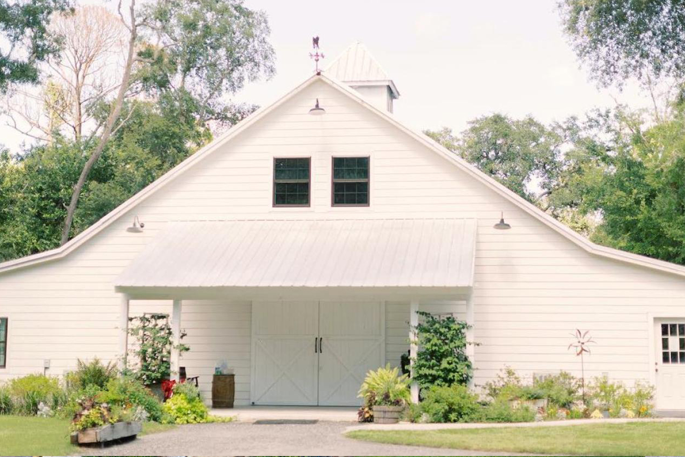 Chandler Oaks Barn wedding venue exterior near St. Augustine FL, elegant white painted barn with metal roof, barn doors open, garden plantings and live oak trees surrounding