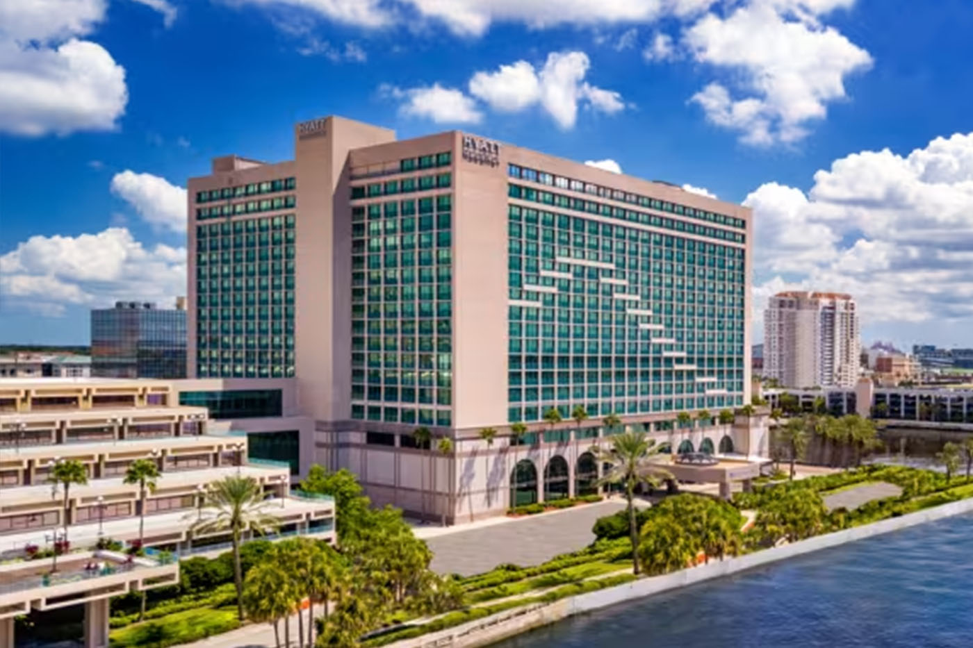 Hyatt Regency Jacksonville Riverfront hotel exterior aerial view, large glass tower on the St. Johns River, downtown Jacksonville skyline, palm trees along the waterfront