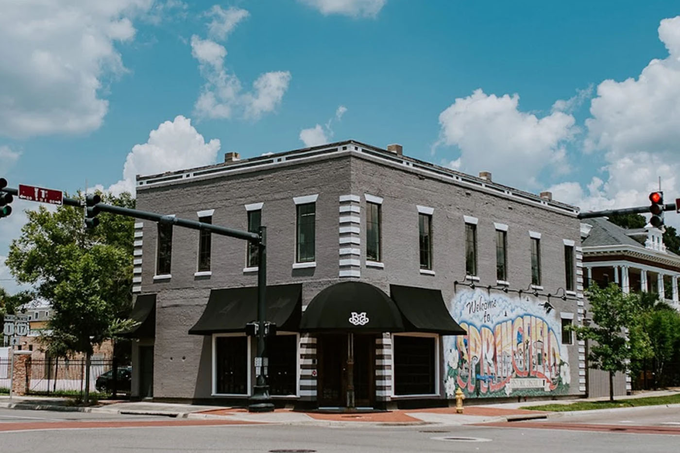Brick and Beam event venue exterior in Historic Springfield District Jacksonville FL, gray brick corner building with black awning, Welcome to Springfield mural on side wall