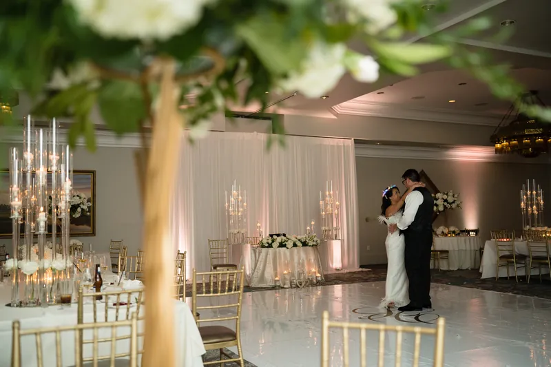Couple sharing a slow dance on the white dance floor at Casa Monica Hotel in St. Augustine FL, white drape backdrop, tall crystal candelabras, gold chiavari chairs, pink uplighting