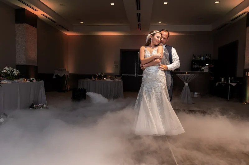 Bride and groom sharing their first dance on the dance floor at Embassy Suites St. Augustine FL, dramatic dry ice fog effect surrounding them, warm uplighting, ballroom reception setup