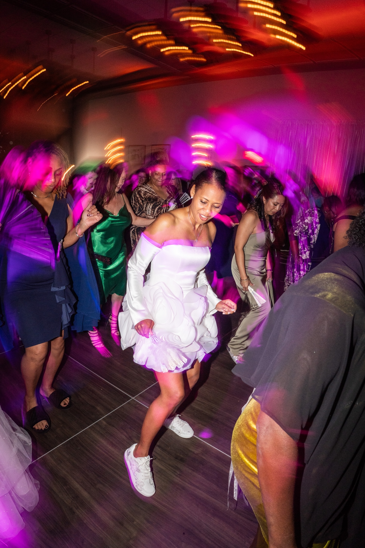 Packed dance floor at Embassy Suites St. Augustine wedding reception, purple and pink uplighting, guests dancing under pendant chandelier lights