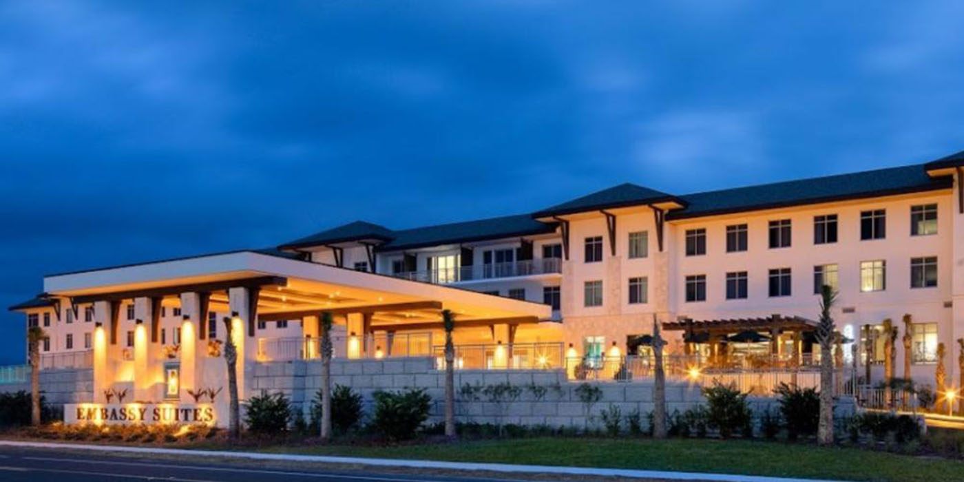Embassy Suites St. Augustine hotel exterior at dusk, illuminated entrance canopy and palm trees, Embassy Suites sign visible, waterfront hotel building lit up at night