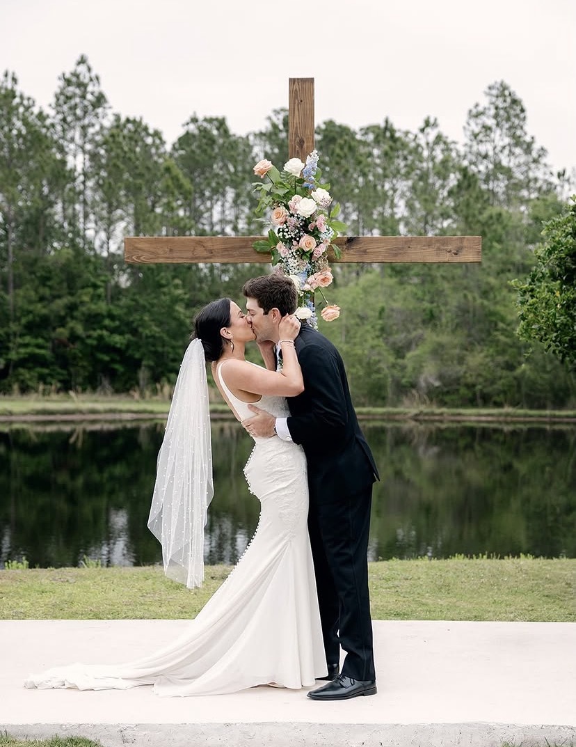 Couple sharing a kiss at the cross altar ceremony space at The Manor at 12 Oaks with a pond and lush treeline reflecting in the water behind them