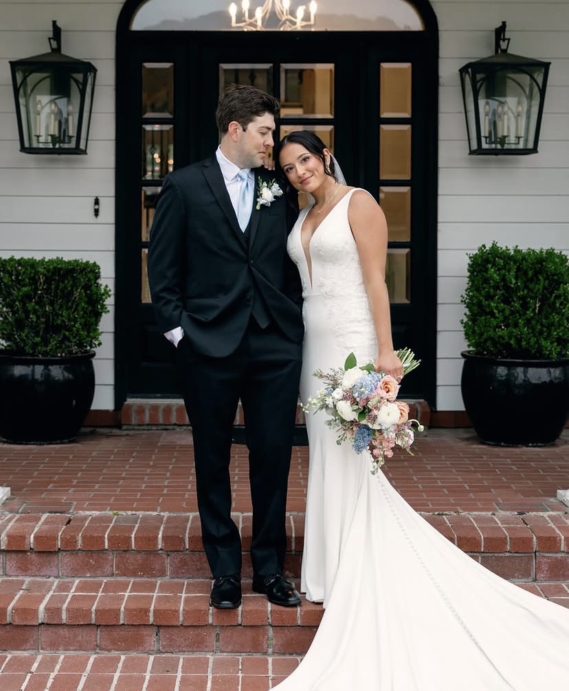 Bride and groom posing in front of the arched black door entrance of The Manor at 12 Oaks Green Cove Springs FL, lantern sconces and boxwood planters framing the Manor facade