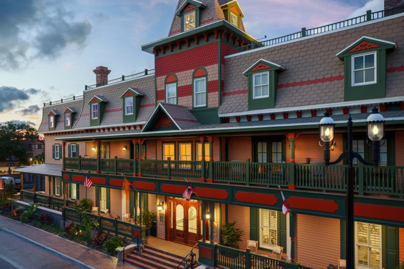 Renaissance St. Augustine Historic Downtown Hotel exterior at dusk, Victorian-era building with green and red trim, wrap-around balconies and gas lanterns lit up in the historic district