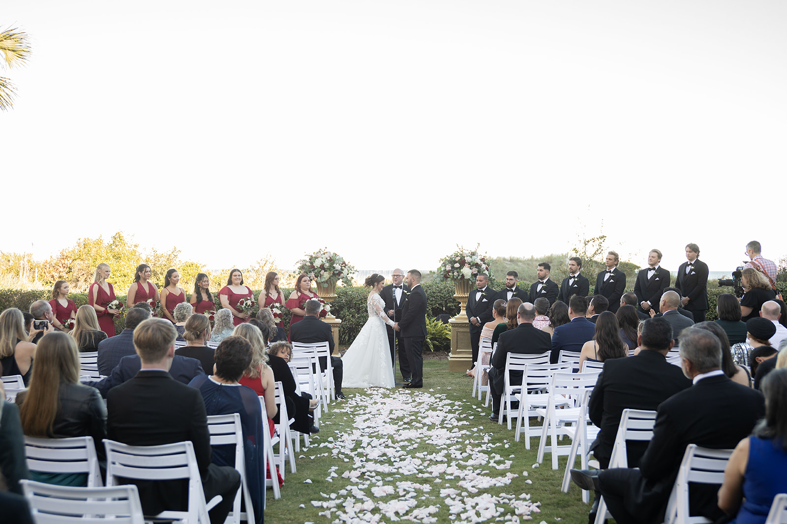 Outdoor oceanfront wedding ceremony on the lawn at Ritz-Carlton Amelia Island FL with full wedding party, white chairs, and Atlantic Ocean in the background — Footloose Entertainment wedding DJ