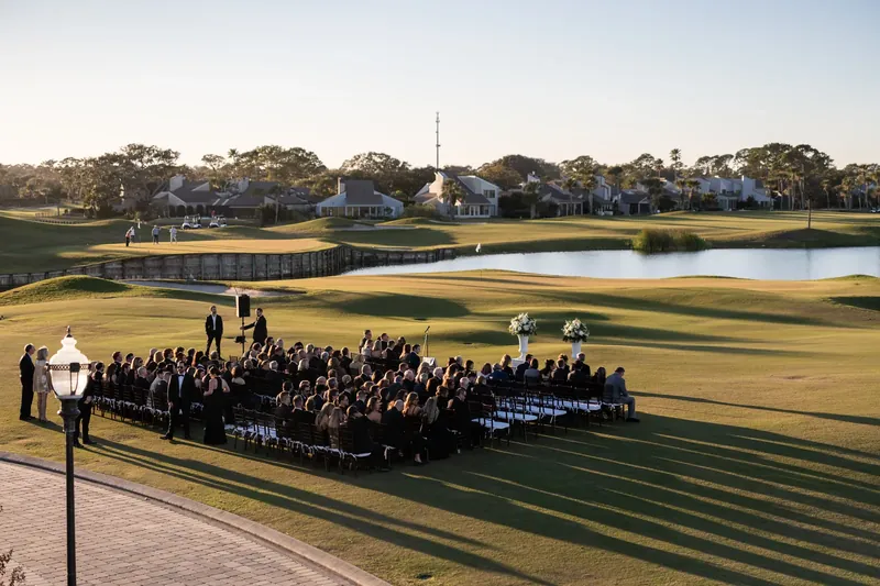Elevated view of outdoor wedding ceremony on the golf course at Sawgrass Marriott in Ponte Vedra Beach FL, rows of seated guests, white floral arrangements, lake and fairway in the background