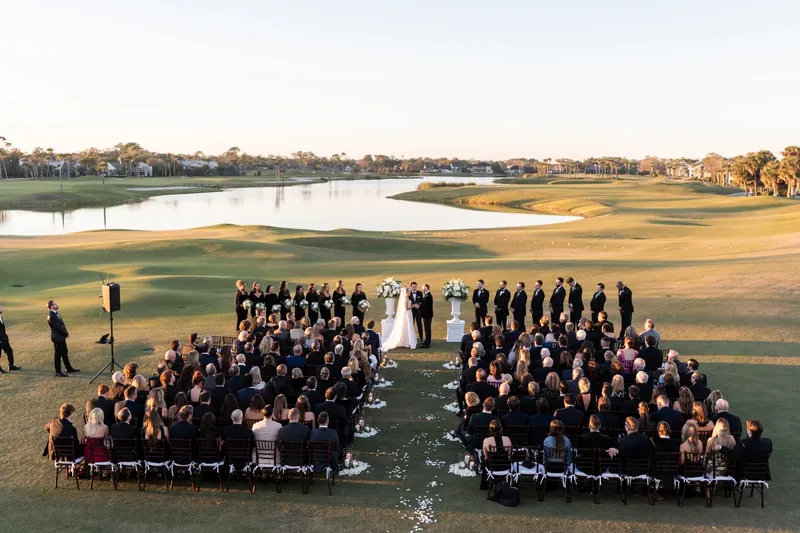 Aerial view of wedding ceremony on the Sawgrass Marriott golf course at golden hour, bride and groom at the altar, guests seated in rows with lake and fairway views