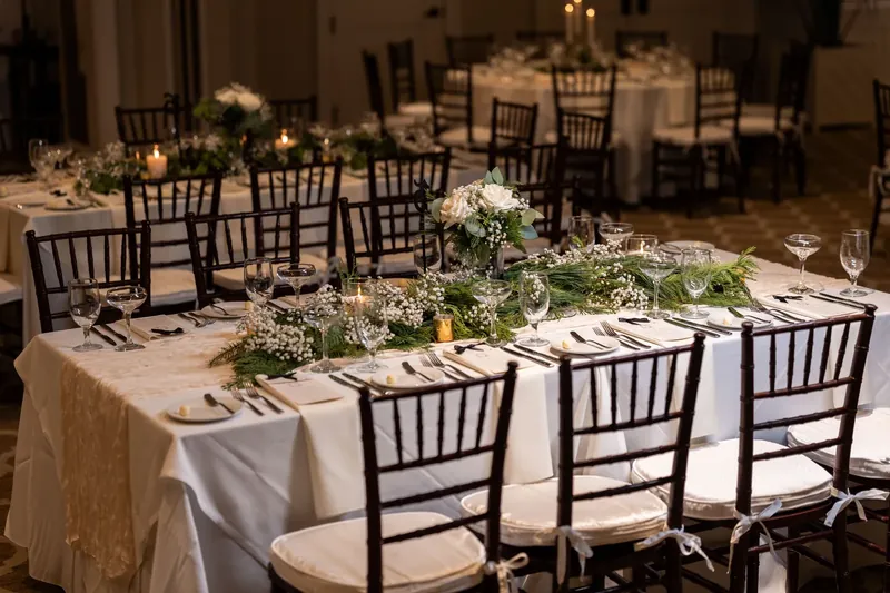 Elegantly set reception table at Sawgrass Marriott in Ponte Vedra Beach FL, dark chiavari chairs, white linens, greenery and white rose runner, candles, ballroom reception in background