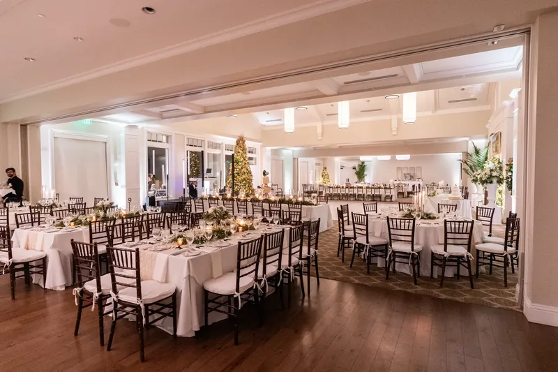 Wide interior shot of a Sawgrass Marriott ballroom set for a wedding reception in Ponte Vedra Beach FL, dark hardwood floors, white linens, dark chiavari chairs, coffered ceiling, soft uplighting