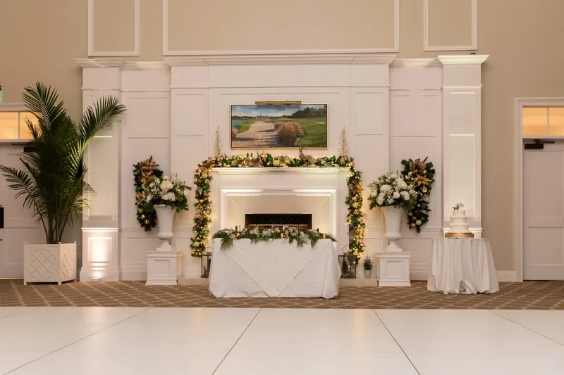 Sweetheart table set in front of a white fireplace mantel at Sawgrass Marriott in Ponte Vedra Beach FL, white dance floor, holiday floral arrangements, palm trees, elegant ballroom setting