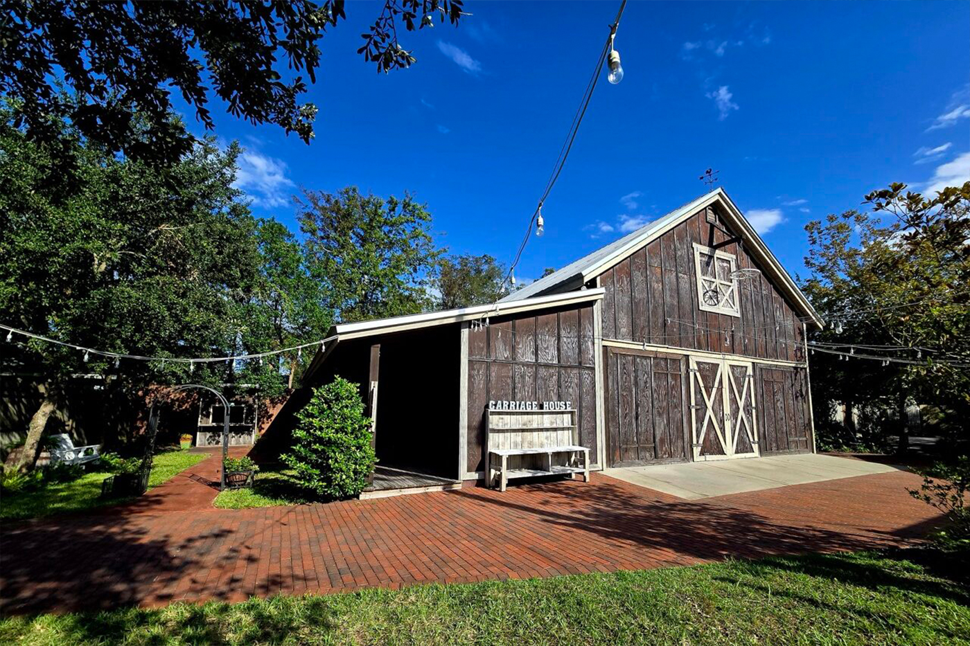 The Carriage House rustic barn wedding venue near St. Augustine FL, weathered wood barn exterior with barn doors, brick patio, string lights and live oak trees