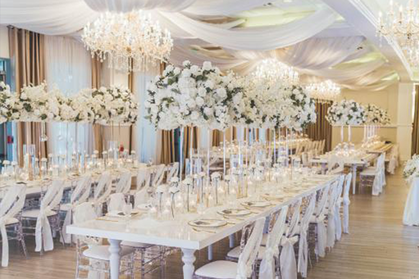 The Legacy at World Golf Village ballroom set for a wedding reception near St. Augustine FL, white draped ceiling, crystal chandeliers, tall white floral centerpieces, acrylic chairs
