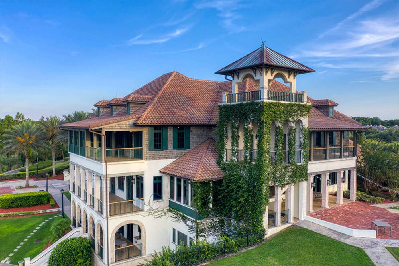 The Palencia Club wedding venue aerial view in St. Augustine FL, Mediterranean-style clubhouse with terra cotta roof, ivy-covered tower, golf course and palm trees surrounding the building