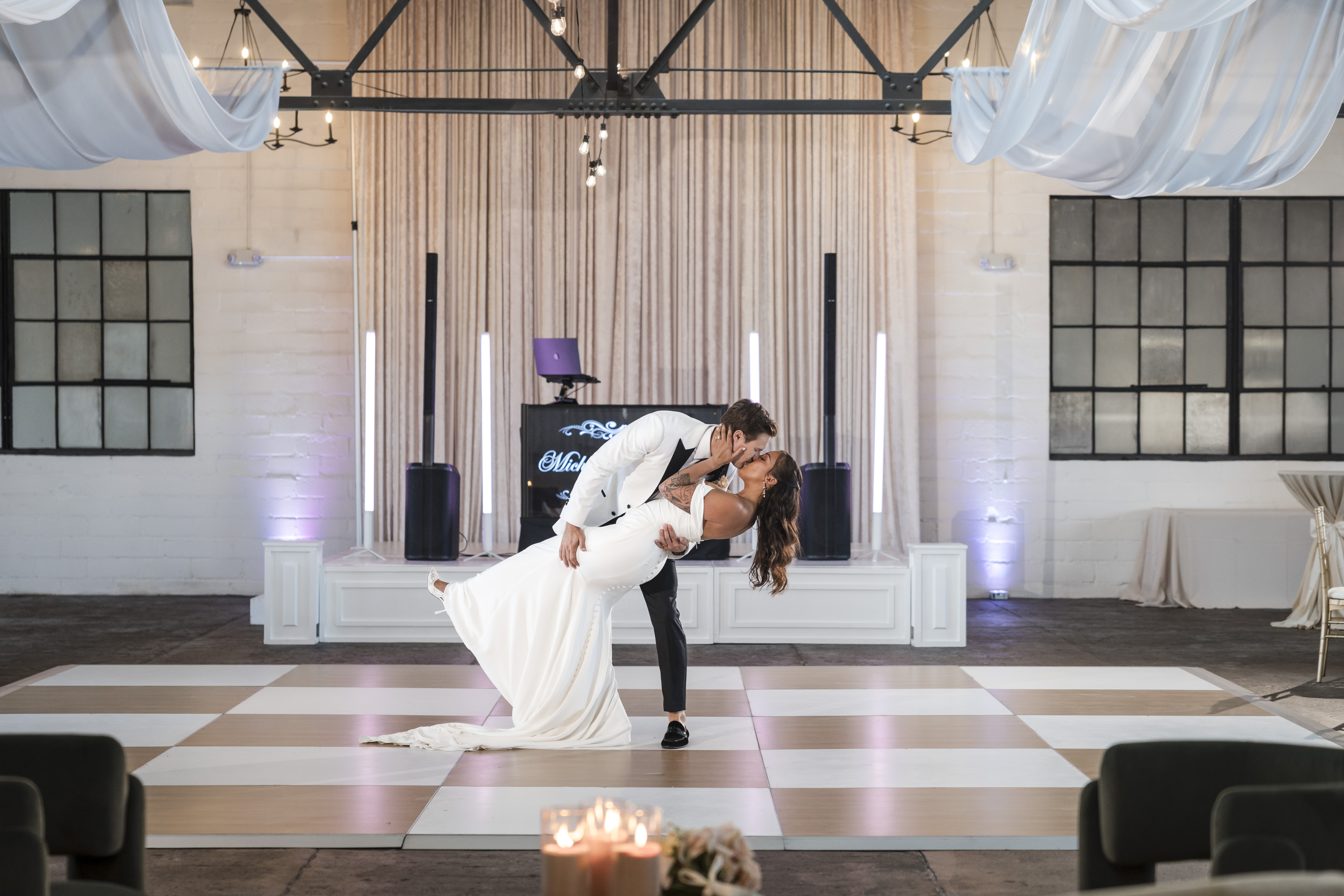 Couple doing a dip kiss on the checkered dance floor at The Venue Hastings with Footloose Entertainment DJ booth and monogram display behind them
