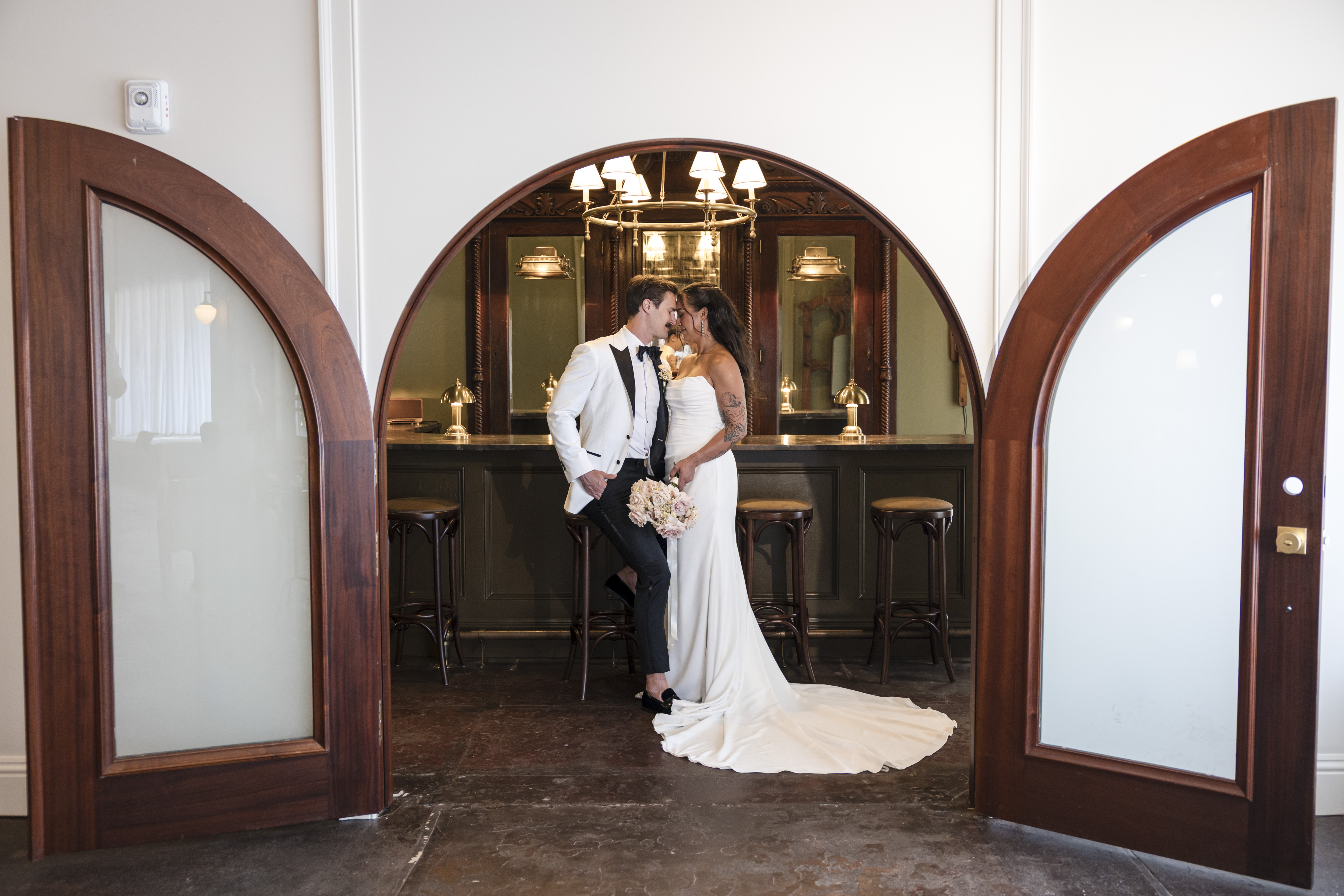 Couple standing in the arched doorway of the bar and lounge space at The Venue Hastings framed by mahogany arched double doors
