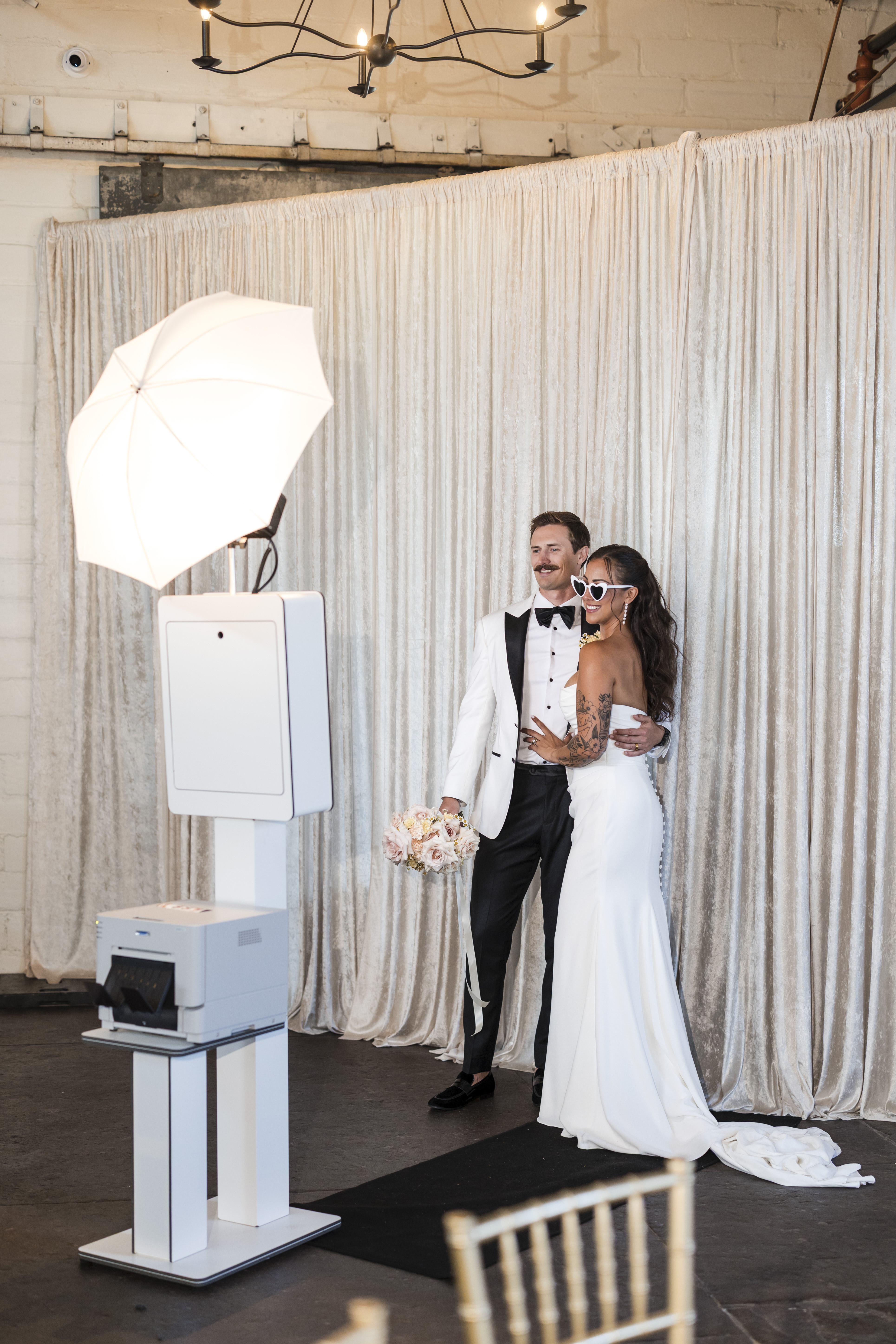 Couple at Footloose Entertainment open-air photobooth at The Venue Hastings, bride wearing heart sunglasses and laughing