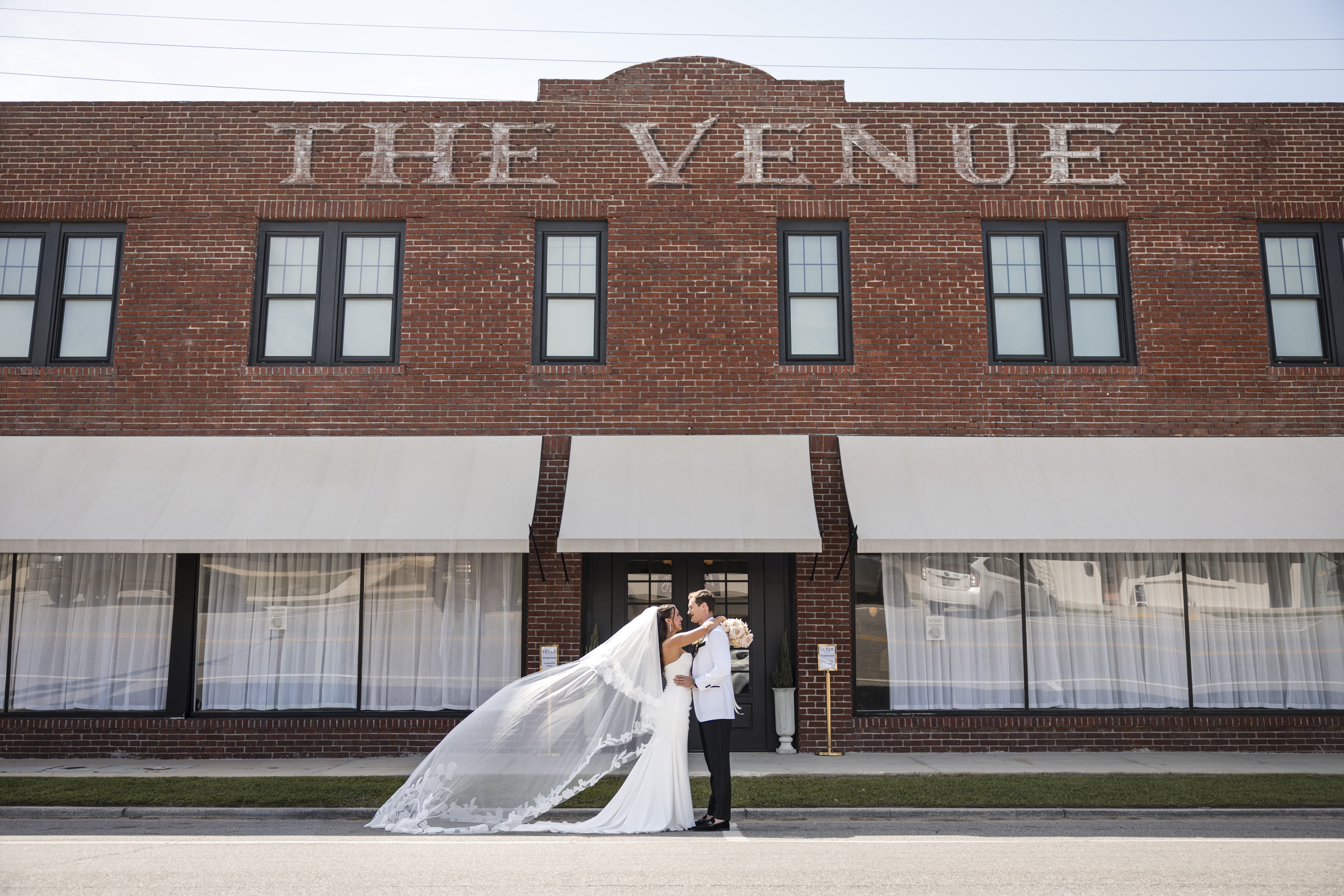Couple kissing in front of The Venue Hastings historic brick building in downtown Hastings FL with veil flowing in the wind
